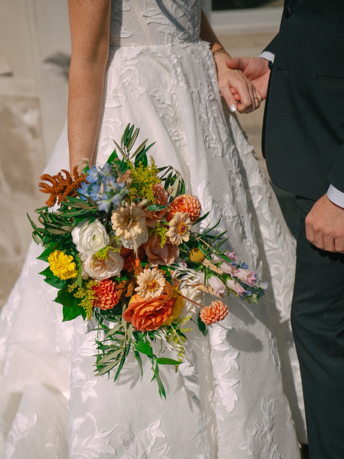 Lauren and Adam holding hands with a colorful wedding bouquet