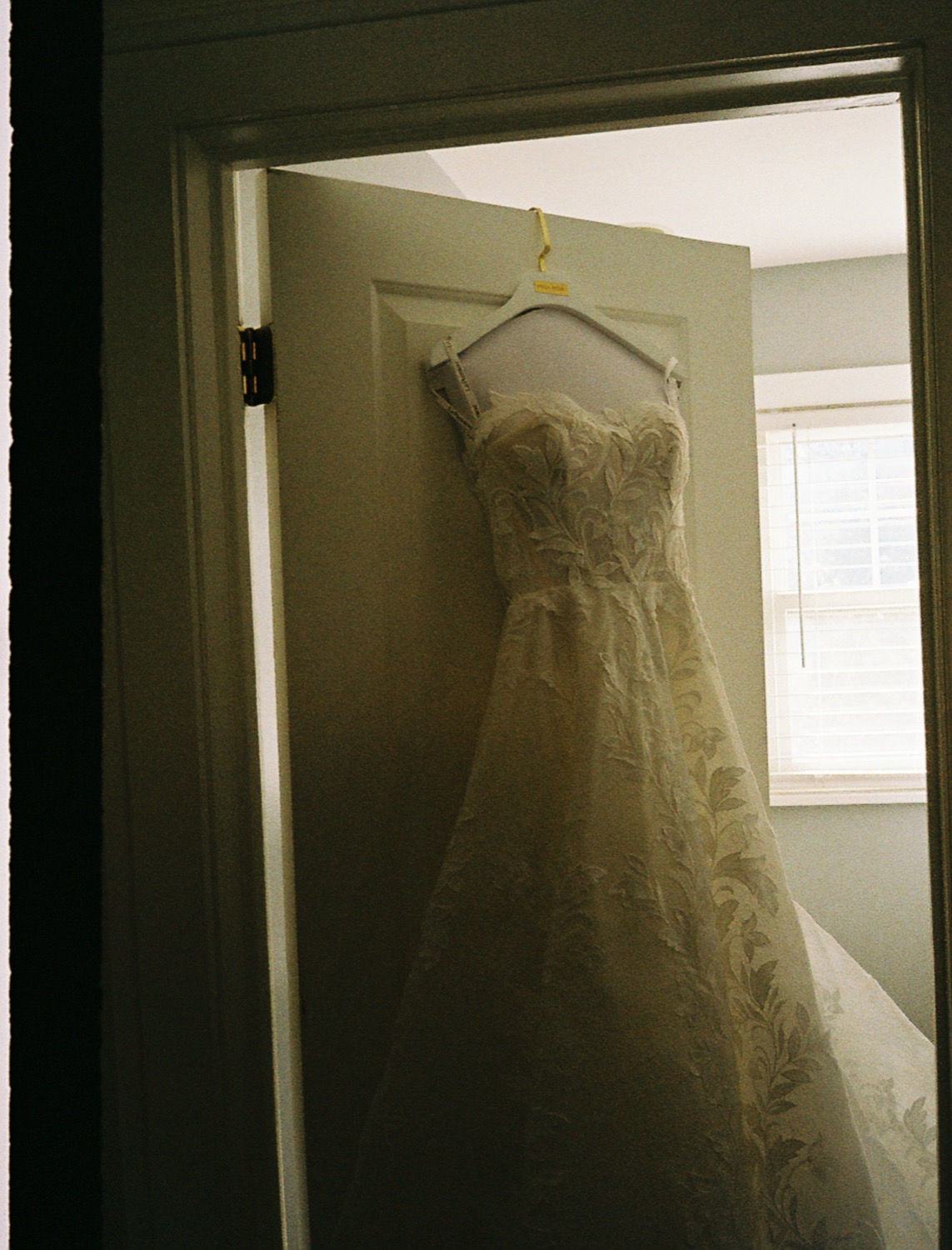 Lauren's embroidered wedding dress hanging by a window